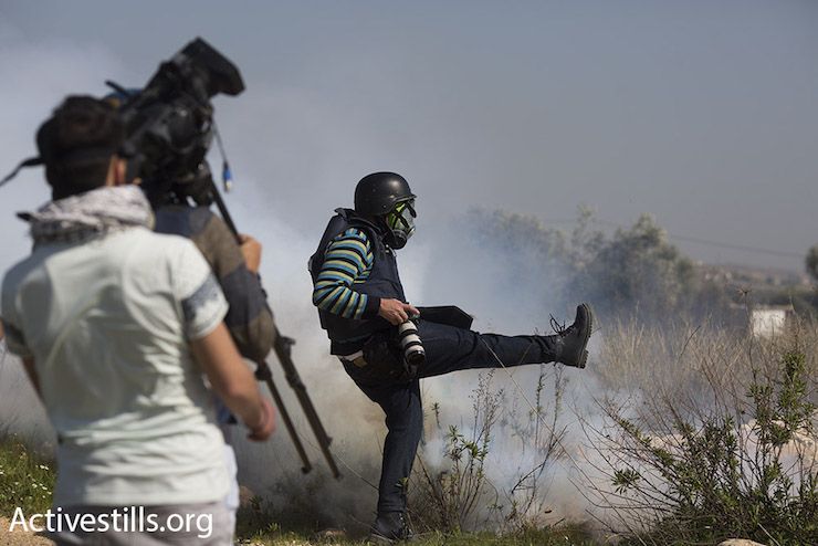 A press photographer kicks away a tear gas canister that Israeli troops fired toward a group of journalists, Bil’in, February 19, 2016. (Oren Ziv/Activestills.org)