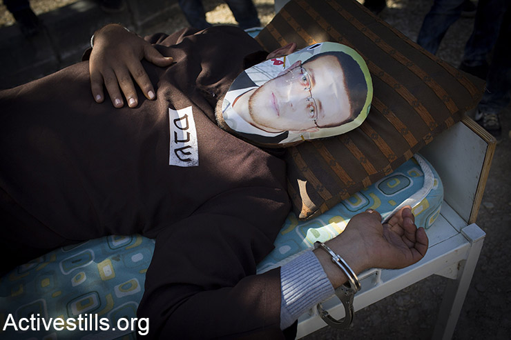 A Palestinian man lying on a bed wears a face covering depicting hunger striking Palestinian journalist Mohammed al-Qiq, on February 19, 2016, during a demonstration protest marking 11 year for the struggle against the wall in the West Bank village of Bilin, near Ramallah. Israel's Supreme Court said on February 16, 2016, the Palestinian hunger striker who has fasted over 80 days must stay in the northern Israeli hospital where he is being held, after a compromise bid failed. (Activestills.org)