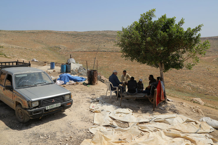 Residents of Khirbet Tana take shelter from the sun under a tree following the Israeli army demolished their homes and other structures earlier in the day, West Bank, April 7, 2016. (Ahmad al-Bazz / Activestills.org)