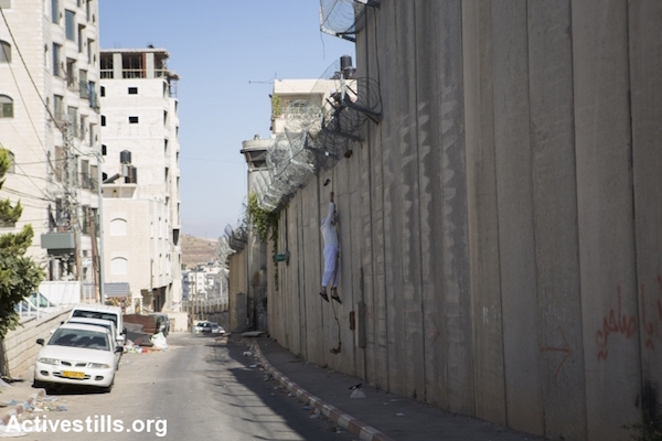 A Palestinian man descends into the East Jerusalem neighborhood of Beit Hanina after climbing over the wall from the West Bank village of a-Ram, July 3, 2015. (File photo by Oren Ziv/Activestills.org)