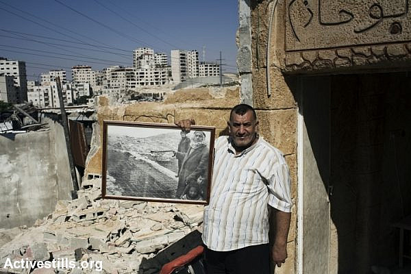 A Palestinian father stands in the ruins of his son's family home a few hours after it was demolished by Israeli authorities, East Jerusalem, May 20, 2013. He is holding a portrait from 1983 in which he and his own father are seen standing near their demolished home in the Anata neighborhood. Seven family members, including 5 children were displaced due to the demolition. (Activestills.org)
