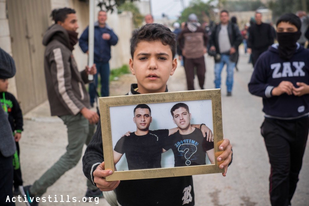A Palestinian boy holds a pictures showing photos of prisoners from the village during the weekly protest in Kafr Qaddum, a West Bank village located east of Qalqiliya, December 19, 2014. 