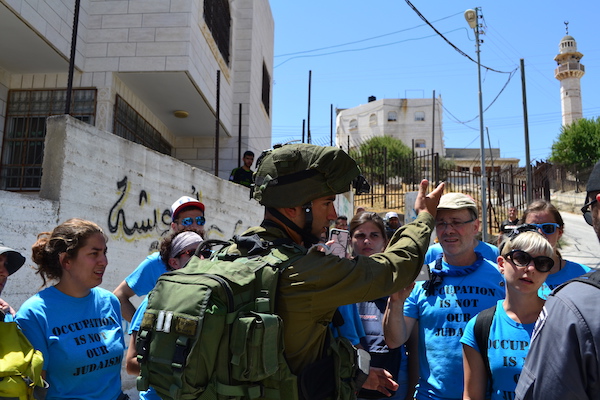 An Israeli soldier attempts to stop activists with the Center for Jewish Non-Violence in the West Bank city of Hebron, July 15, 2016. (Dahlia Scheindlin)