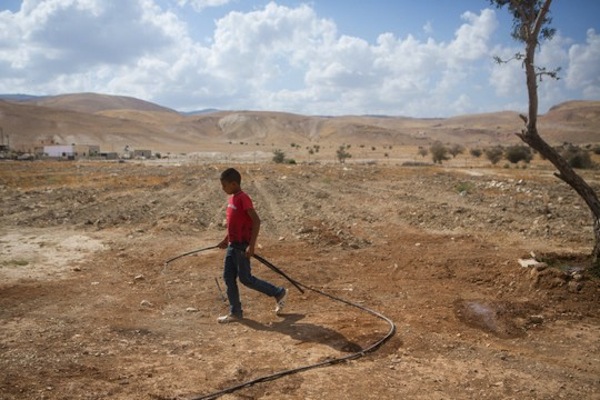 A young Palestinian boy from the West Bank village of Fasayil, Jordan valley, seen walking with a water pipe in the village. May 14, 2015. (Miriam Alster/Flash90)