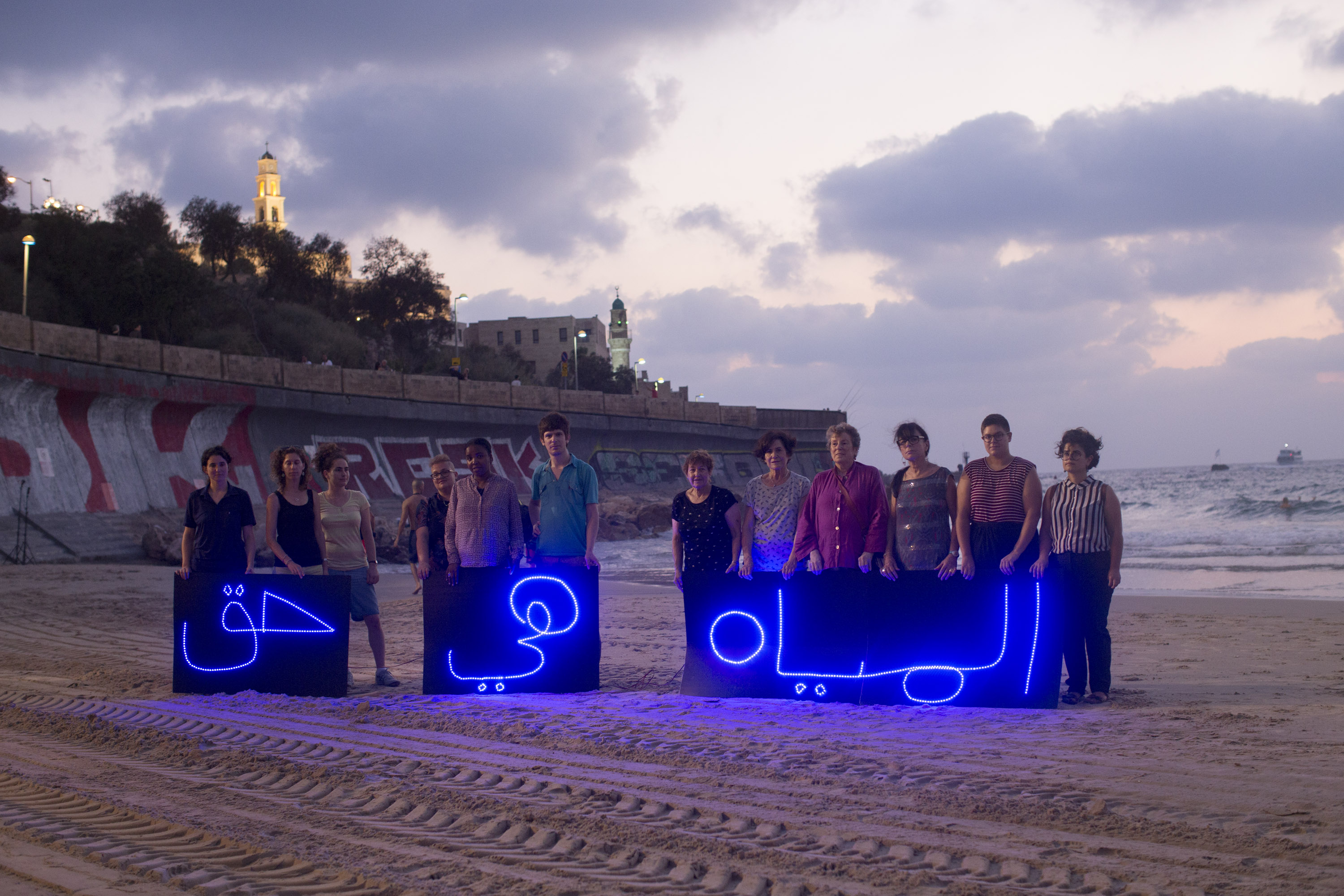Activists hold illuminated Arabic letters that spell out "Water is a basic right" as part of an international light installation coordinated by the "Water Coalition," calling for equal water rights for Palestinians, August 14, 2016. (Oren Ziv/Activestills.org)