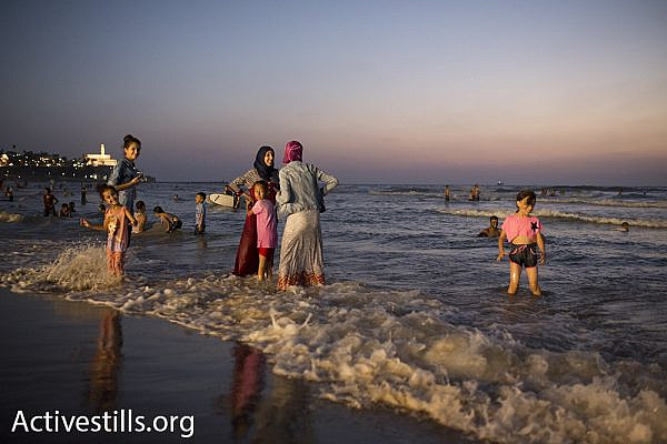 Palestinian women and children wade in the sea during Eid al-Adha, September 14, 2016. (Oren Ziv/Activestills.org) The Old City of Jaffa is seen in the background.