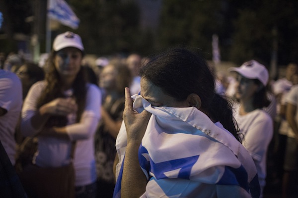 An Israeli woman breaks into tears as she covers herself in an Israeli flag during a rally marking two years since Israeli soldier Oron Shaul was taken captive by Hamas, at the protest tent outside the Prime Minister Benjamin Netanyahu's residence, Jerusalem, July 20, 2016. (Hadas Parush/Flash90)
