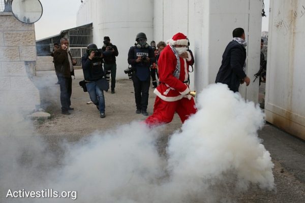 A protester dressed as Santa Claus runs from a cloud of tear gas shot by Israeli Border Police, Bethlehem, West Bank, December 23, 2016. (Activestills)