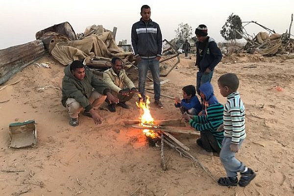 Residents of Bir Hadaj warm themselves around a fire after homes in the village were demolished. (Rami Younis)