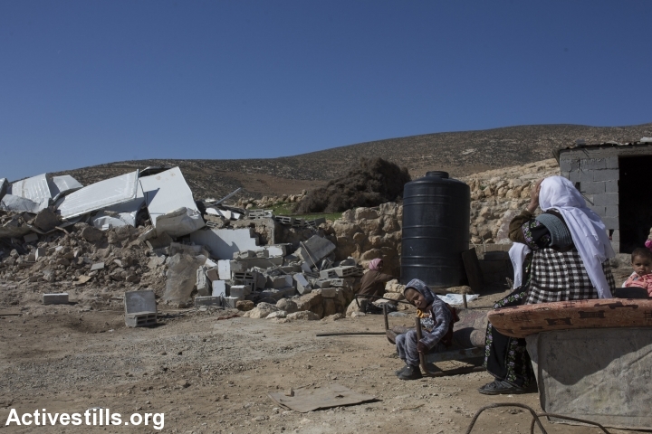 Palestinians sit next to their demolished home after it was torn down by Israeli bulldozers in the village of Khirbet al-Halawah, 'Firing Zone 918,' south Hebron Hills, West Bank, February 3, 2016. (Oren Ziv/Activestills.org)