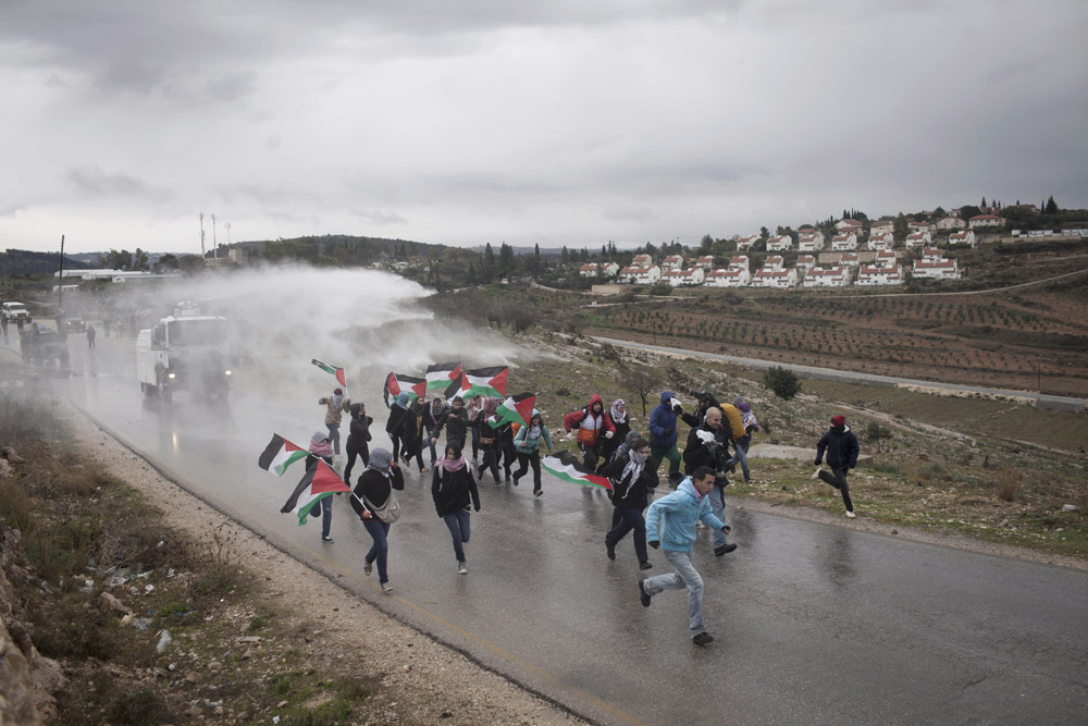 Palestinian, international and Israeli activists flee an Israeli army ‘skunk’ truck at an anti-occupation protest in the West Bank village of Nabi Saleh, January 13, 2012. (Activestills.org)