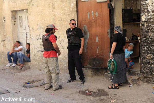 File photo of private security guards escorting a Jewish settler family in the East Jerusalem neighborhood of Silwan as Palestinian youths look on. (Anne Paq/Activestills.org)