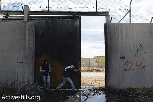 Palestinian youths force open a gate in the Israeli separation wall, built on land belonging to the village of Bil’in, which leads to the Israeli settlement of Modi’in Ilit, also built on village land, February 17, 2017. (Oren Ziv/Activestills.org)