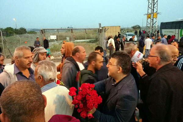 Hadash MK Yousef Jabareen hands out flowers to Palestinian laborers at the Eyal checkpoint. (Courtesy)
