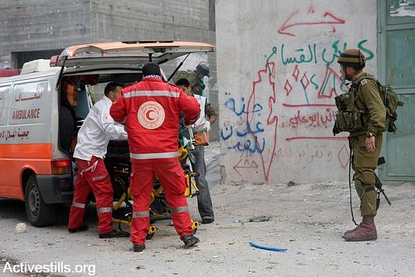 An Israeli army officer watches as Palestinian medics evacuate a wounded Palestinian man in Bethlehem. (Anne Paq/Activestills.org)