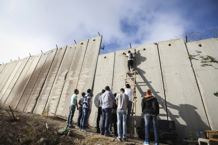 Palestinians try to climb over the separation wall at the Qalandyia checkpoint between the West Bank city of Ramallah and Jerusalem on their way to attend the last Friday prayers in Jerusalem's al-Aqsa mosque during Muslim holy month of Ramadan, Friday, July 1, 2016. (Photo by Flash90)