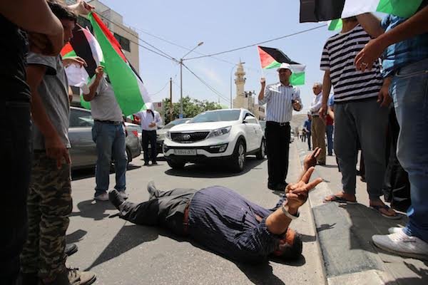 A Palestinian demonstrator gestures while lying on the ground during a protest in solidarity with hunger striking Palestinian prisoners, near Huwwara, West Bank, May 18, 2017. (Ahmad al-Bazz/Activestills.org)