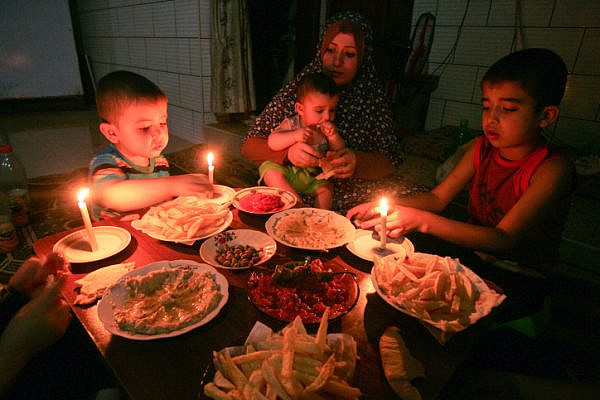 A Palestinian family eats dinner by candlelight at their makeshift home in the Rafah refugee camp, in the southern Gaza Strip, during a power outage on June 12, 2017. (Abed Rahim Khatib/ Flash90)
