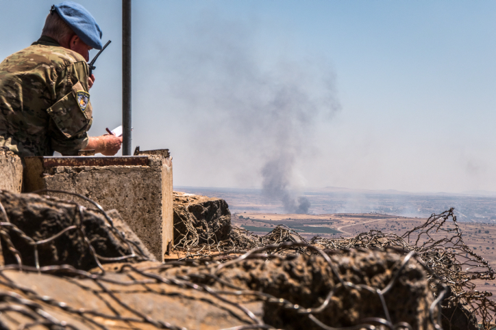 A UN observer looks at a lookout point as smoke rising at a Syrian village near the Israeli-Syrian border in the Golan Heights during fights between the rebels and the Syrian army, June 25, 2017. (Basel Awidat/Flash90)