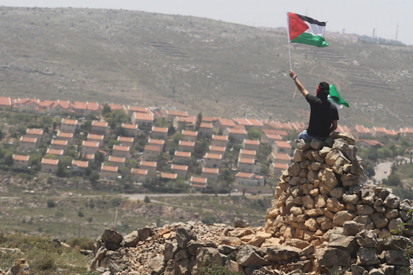 A Palestinian demonstrator from the West Bank village of Deir Jarir, northeast of Ramallah, waves a Palestinian flag as he sits on a pile of rocks during clashes with Israeli soldiers following a march against construction on Palestinian land by members of the Jewish settlement of Ofra on April 26, 2013. (Issam Rimawi/FLASH90)