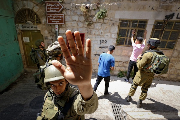 An Israeli soldier attempts to block the view of a photographer as Israeli soldiers search Palestinian men in the West Bank city of Hebron, June 22, 2017. (Wisam Hashlamoun/Flash90)