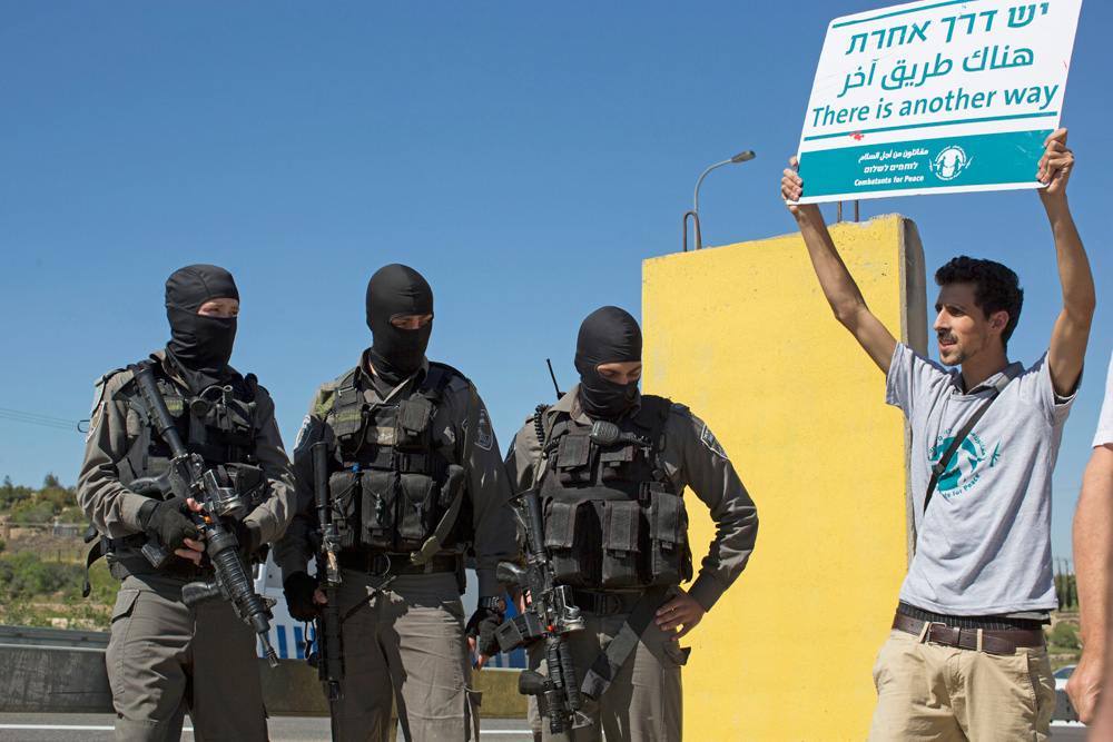 A left-wing Israeli protester stands next to masked Israeli riot police at an anti-occupation demonstration in the West Bank, April 1, 2016. (Oren Ziv/Activestills.org)
