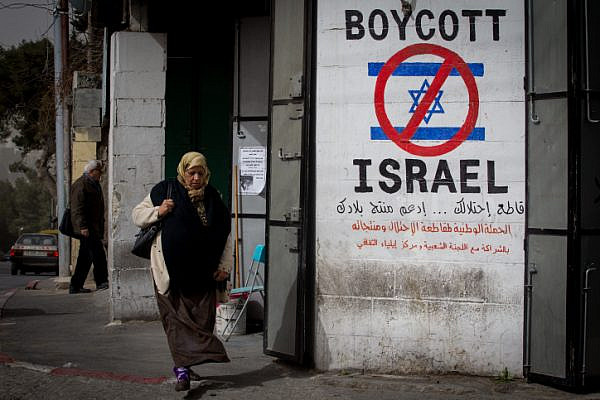 A Palestinian woman walks by a grafitti sign calling to boycott Israel seen on a street in the West Bank city of Bethlehem on February 11, 2015. (Miriam Alster/Flash 90)
