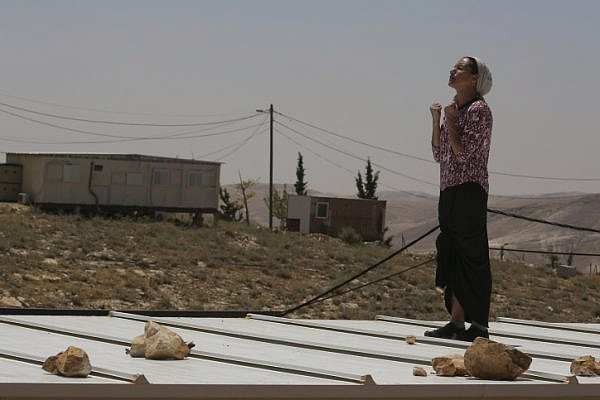A settler stands and prays on top of her home roof during the demolition and evacuation of 10 structures in the Ma'ale Rehavam outpost, West Bank, May 14, 2014. (Nati Shohat/Flash 90)