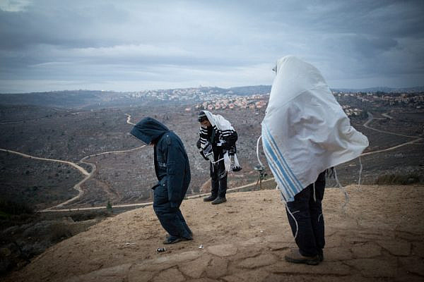 Jewish men pray early in the morning on the hill overlooking Ofra in the Jewish settlement of Amona in the West Bank, December 18, 2016. (Miriam Alster/Flash90)