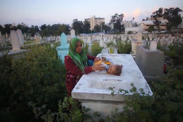 A woman with her baby in a Gaza cemetery. (Photo by Mohammed Abu Nahel)