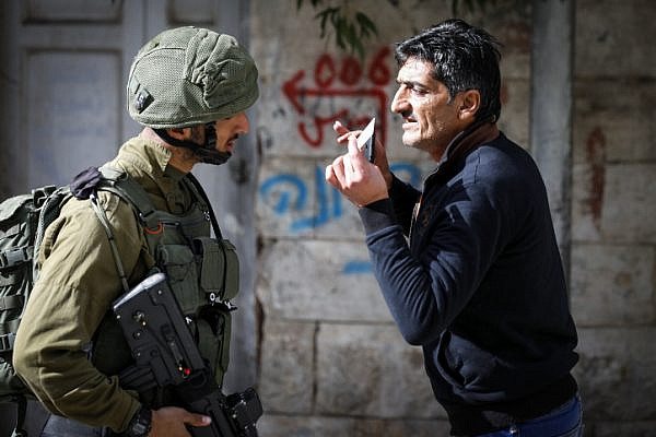 An Israeli soldier checks the ID of a Palestinian man the Old City of Hebron, West Bank, January 14, 2018. (Wisam Hashlamoun/Flash90)