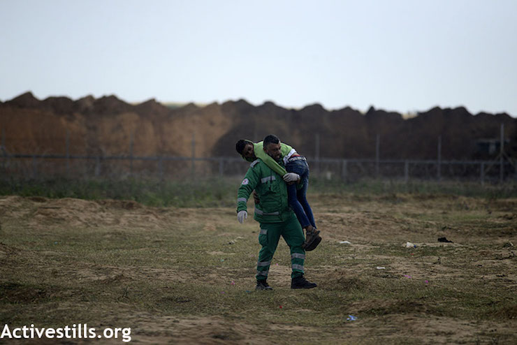 An injured Palestinian man being helped during the Great Return March in Gaza, east of the Jabaliya refugee camp. March 30, 2018. Palestinians tend to a boy injured during the Great Return March in Gaza, east of the Jabaliya refugee camp. March 30, 2018. (Mohammed Emad / Activestills.org)