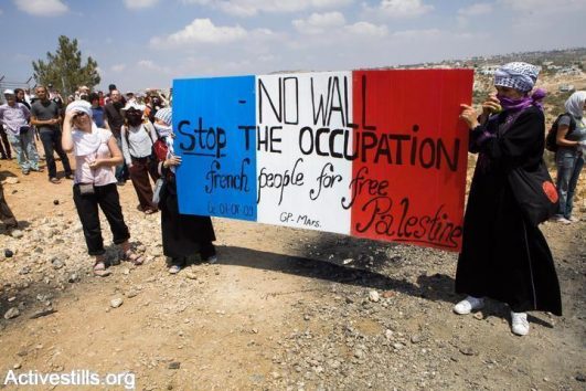Women activisits hold up signs during an action that attempts to dismantle a barbed wire part of the gate of the Seperation Wall in Bil'in, as part of the weekly protest against the Separation Wall and the occupation, West Bank, August 14, 2009. Hundreds of Palestinians, Israeli, and international activists, responded to the Popular Committee's call to resist to participate in the action. (Yotam Ronen/Activestills.org)
