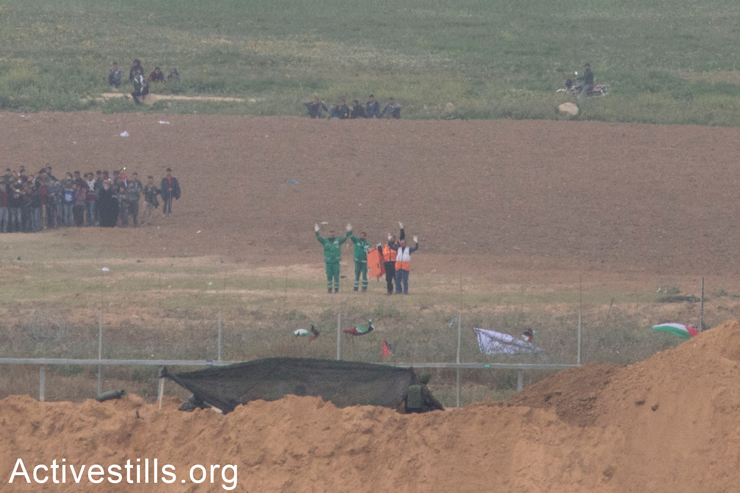 Palestinian medics signal to Israeli soldiers that they are unarmed as they attempt to retrieve wounded Palestinians along the Gaza border fence, seen from the Israeli side, March 30, 2018. (Oren Ziv/Activestills.org)