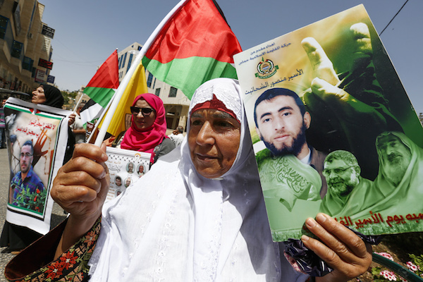 Palestinians hold photos of Palestinian prisoners during a protest to demand the release of their relatives jailed in Israeli prisons, on the Prisoners' Day in the West Bank city of Hebron, on April 17, 2018. (Wisam Hashlamoun/Flash90)