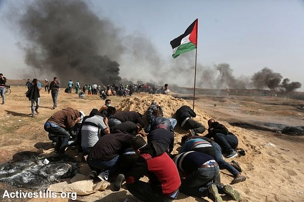 Palestinian protesters take cover behind a dirt mound as Israeli soldiers open fire from across the border in the distance, east of Jabaliya, Gaza Strip, April 6, 2018. Israeli snipers have killed over 30 people and shot over 1,000 others since The Great Return March began a week earlier. (Mohammed Zaanoun/Activestills.org)