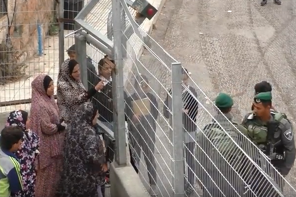 Palestinian women plead with Israeli Border Police officers to open a gate to allow their children to cross through on their way home from school, Hebron, May 13, 2018. (B'Tselem)