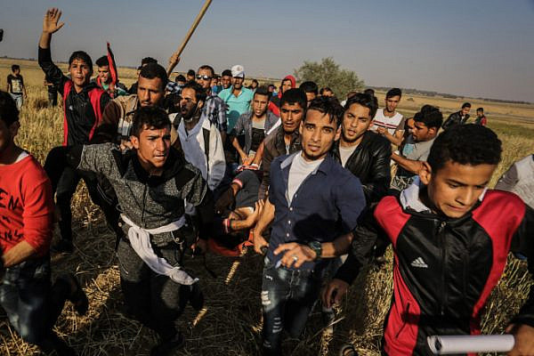 Palestinians carrying a wounded Palestinian man at the Israel-Gaza border, during the Great Return March, Khan Younis in the southern Gaza Strip, April 15, 2018. (Abed Rahim Khatib/Flash90)