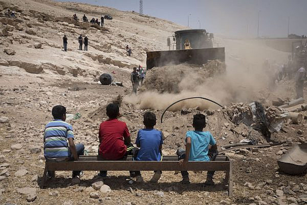 Residents of the Bedouin village Khan al-Ahmar look on as a bulldozer paves an access road to be used by Israeli forces in the imminent demolition of the West Bank hamlet, July 4, 2018. (Oren Ziv)
