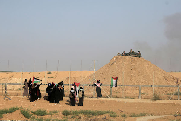 Palestinian women hang a Palestinian flag in range of Israeli snipers during a women's march toward the Israel-Gaza fence, east of Gaza City, July 3, 2018. (Mohammad Za’anoun/Activestills.org)