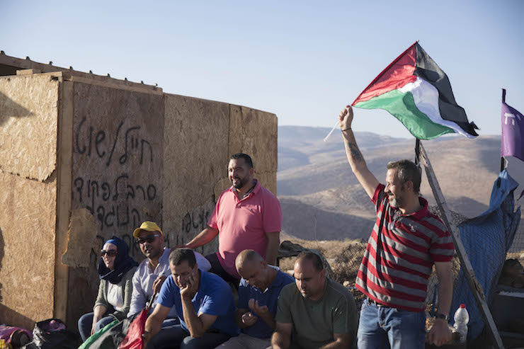 The villagers of Ein Samia wave Palestinian flags at an abandoned structure built by settlers, as part of the notoriously radical Baladim outposts, August 15, 2018. (Oren Ziv/Activestills.org)