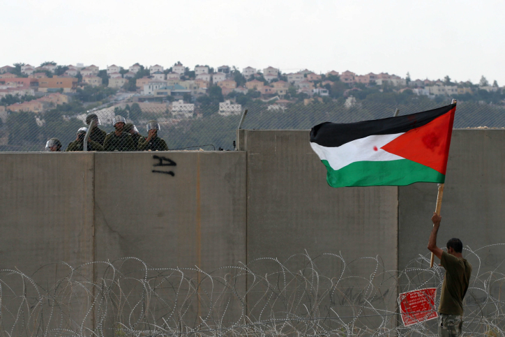 A Palestinian protester holds the Palestinian flag near the Israeli separation wall as Israeli security officers look on during a protest in the West Bank village of Bil'in near Ramallah on September 9, 2011. (Issam Rimawi/Flash90)