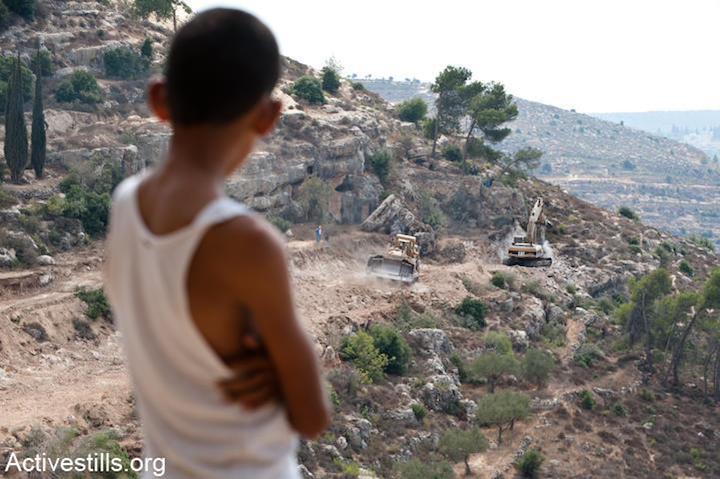 A Palestinian boy watches a bulldozer clearing land for the Israeli separation wall surrounding the West Bank village of Walajeh, September 5, 2011. (Ryan Rodrick Beiler)