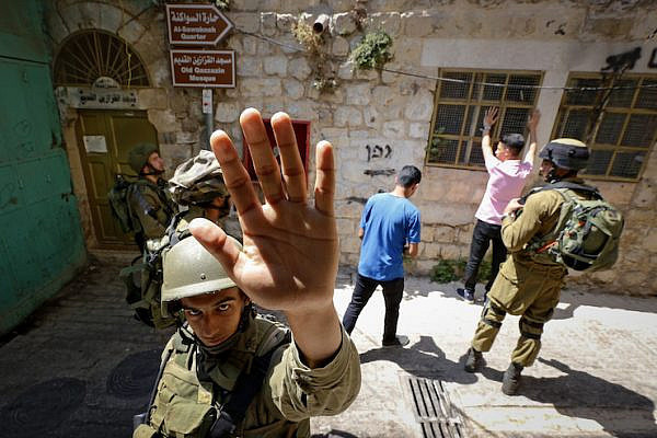 An Israeli soldier attempts to block the view of a photographer as soldiers body search Palestinian men in the West Bank city of Hebron on June 22, 2017. (Wisam Hashlamoun/Flash90)
