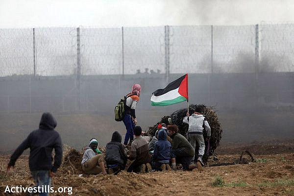 A group of protesters wave a Palestinian flag while trying to take cover during the demonstration, east of Gaza City, March 30, 2019. (Mohammed Zaanoun/Activestills.org)