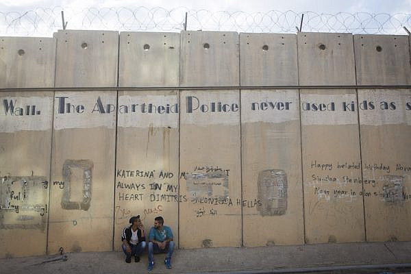 Young Palestinian men sit beneath the separation wall in the West Bank city of Al-Ram, September 29, 2014. (Miriam Alster/Flash90)