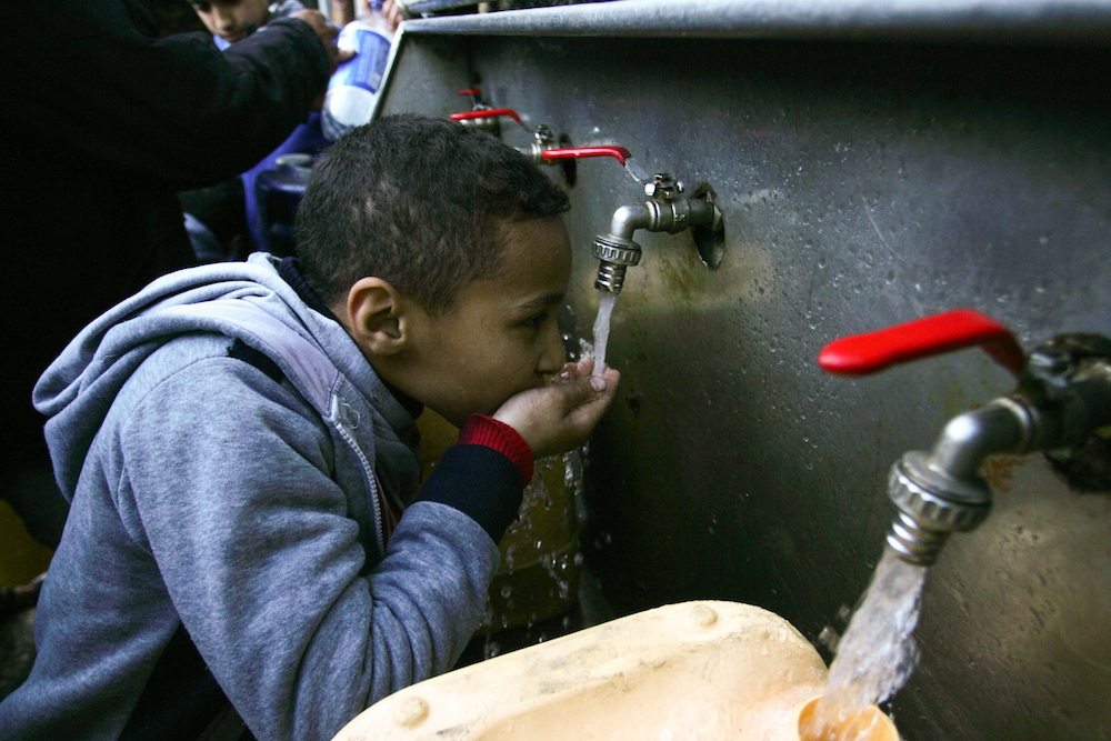 Palestinians fill water from pipes provided by the United Nations Relief and Works Agency (UNRWA) headquarters in the Rafah refugee camp in the southern Gaza Strip, January 6, 2018. (Abed Rahim Khatib/Flash90)