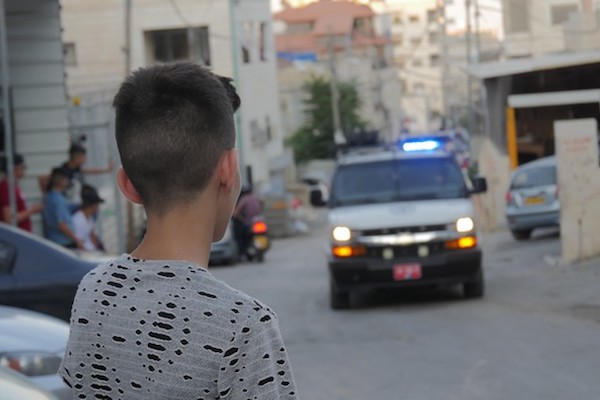 A Palestinian child looks on at a police vehicle in the East Jerusalem neighborhood of Issawiya. (Yuval Abraham)