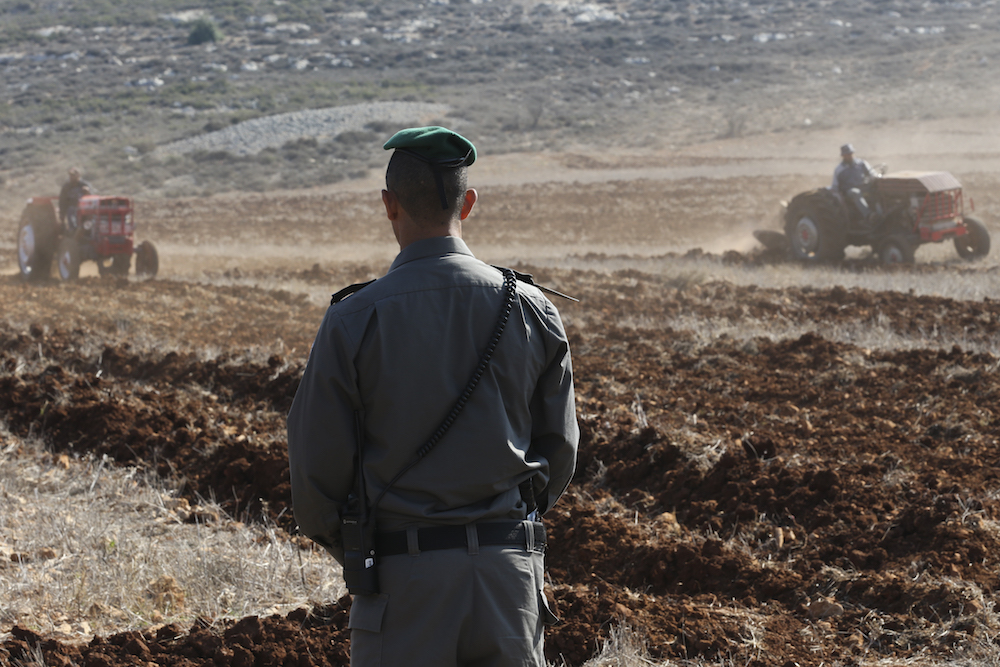An Israeli Border Police officer looks on at Palestinian farmers in the West Bank village of Qusra, November 19, 2013. (Nati Shohat/Flash90)