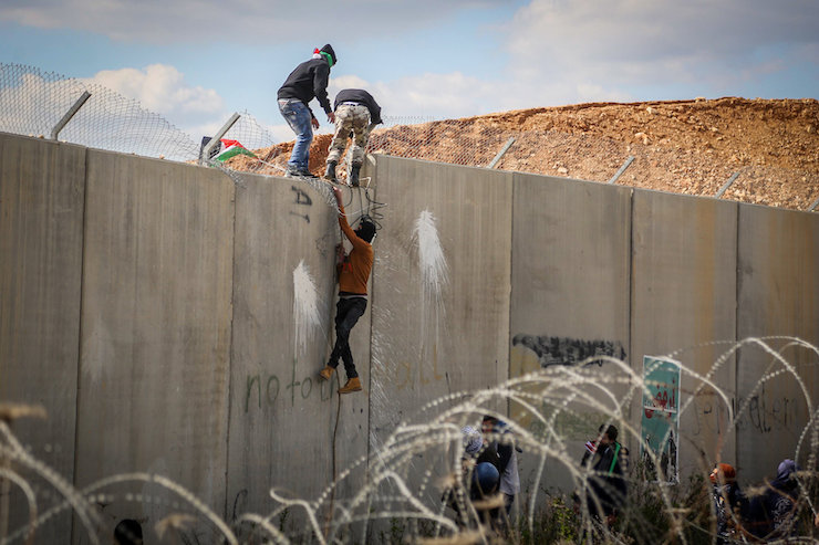 Palestinian protesters climb over the separation barrier in protest of it, in the West Bank village of Bil'in, near Ramallah, Friday, Febraury 17, 2017. (Flash90)